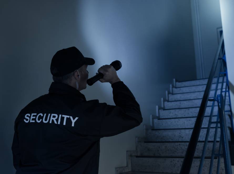 A security guard walks the stairs at night while holding a flashlight.