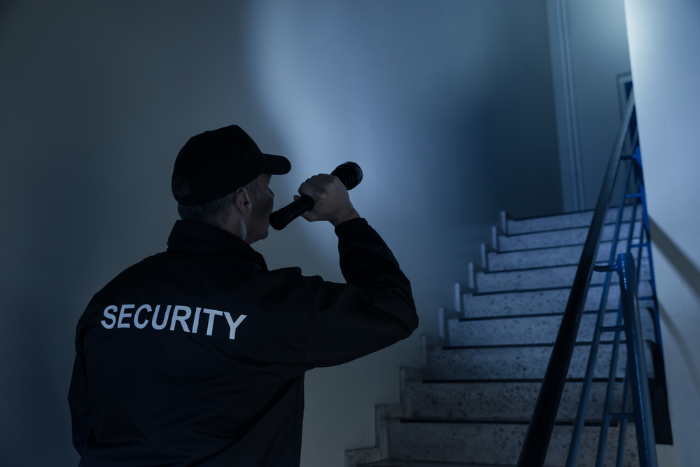 A security guard walks the stairs at night while holding a flashlight.